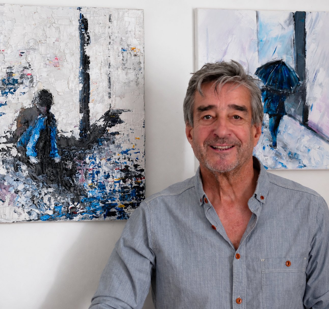 Trevor Chatfield at home, standing in front of two of his paintings